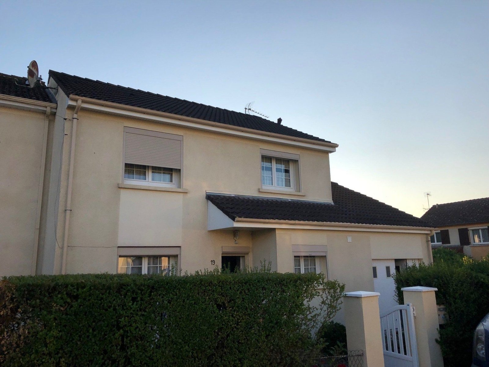 Une maison avec une clôture autour et une voiture garée devant.