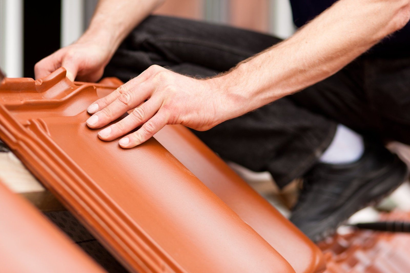 Un homme travaille sur un toit avec des tuiles rouges.